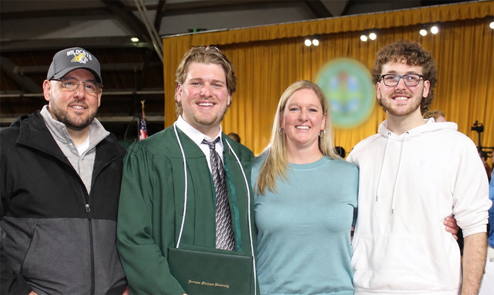 A family of four poses together for a photo at a college graduation ceremony.