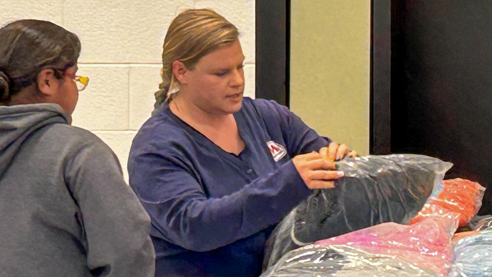 A woman opens a plastic bag with a coat inside.